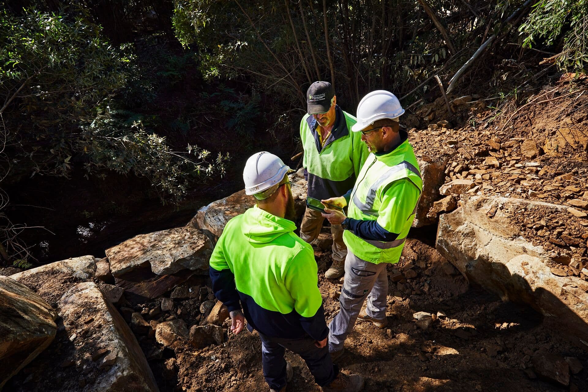 Three workers wearing hard hats and high-visibility shirts beside rocks